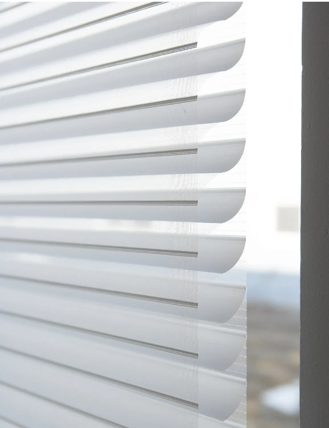 Esta persiana enrollable tiene tablones semi opacos entre dos lienzos traslúcidos. Se puede controlar el paso de la luz con los tablones, o enrollar por completo para revelar el claro de la ventana.